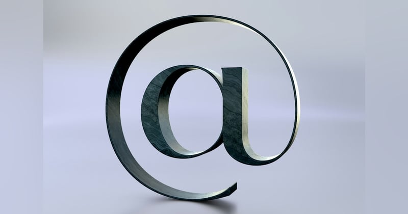3D at sign standing on a light lavender-grey background